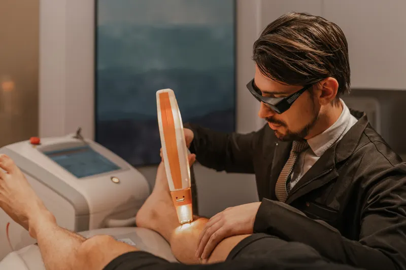 Dr. Rafael Giacobbo aplicando laser na perna de um paciente na clínica