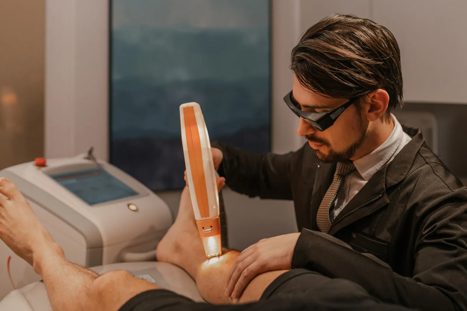 Dr. Rafael Giacobbo aplicando laser na perna de um paciente na clínica